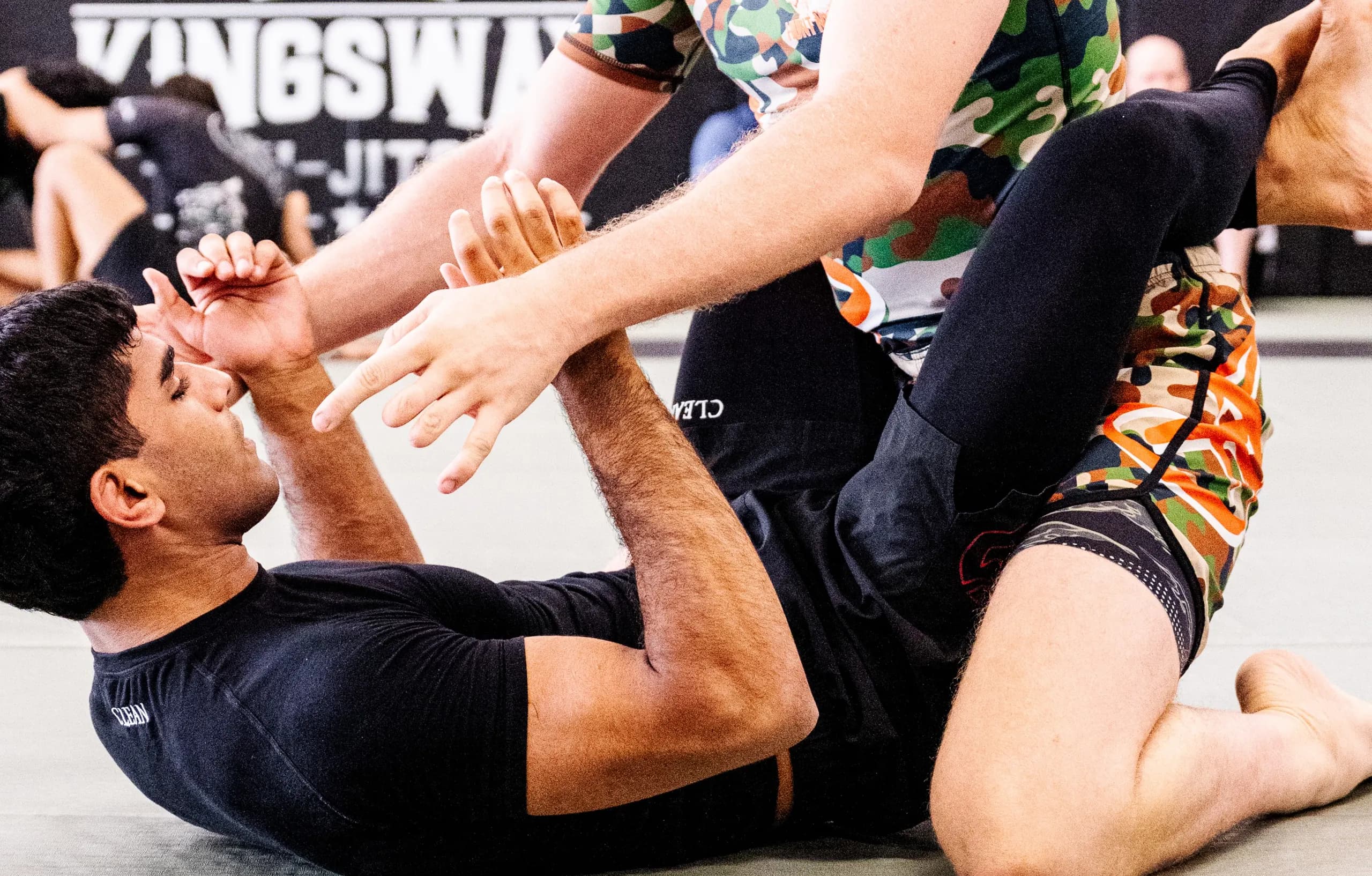 On the mat in the short-sleeve rash guard and spats, one leg raised against a training partner.